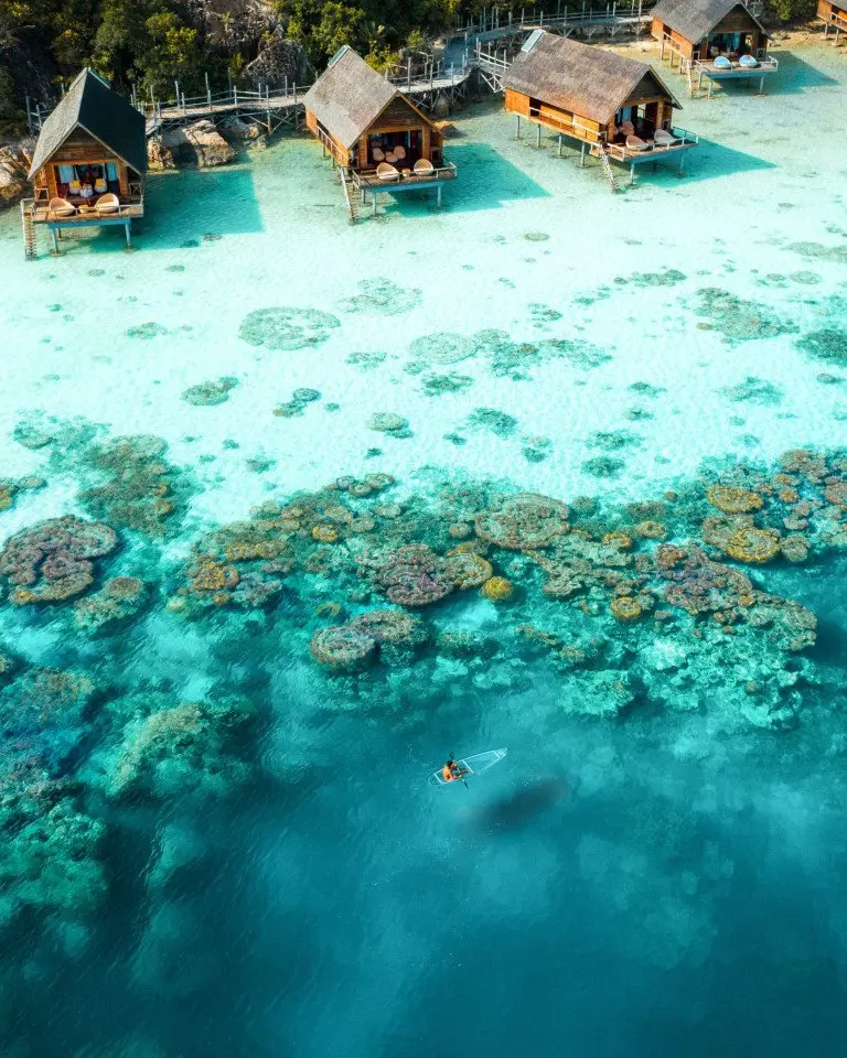 aerial_man_holding_oar_clear_kayaking_coral_reefs_lagoon_from_distance_west_overwater_suites