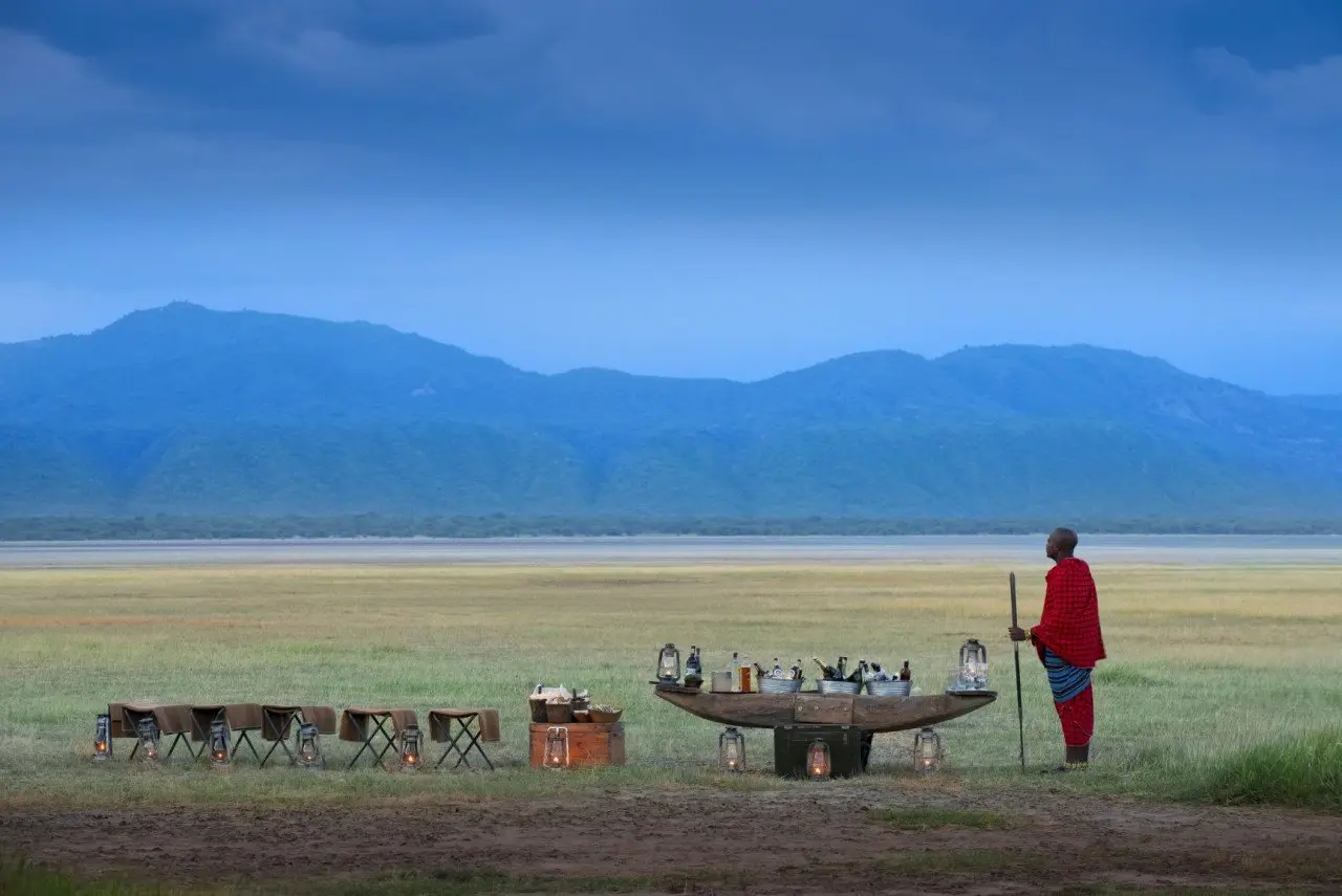 Tanzania-Lake-Manyara-Tree-Lodge-Guest-delight-drink-stop-sundowners-at-sunset-with-Maasai-warrior-at-the-lake-4