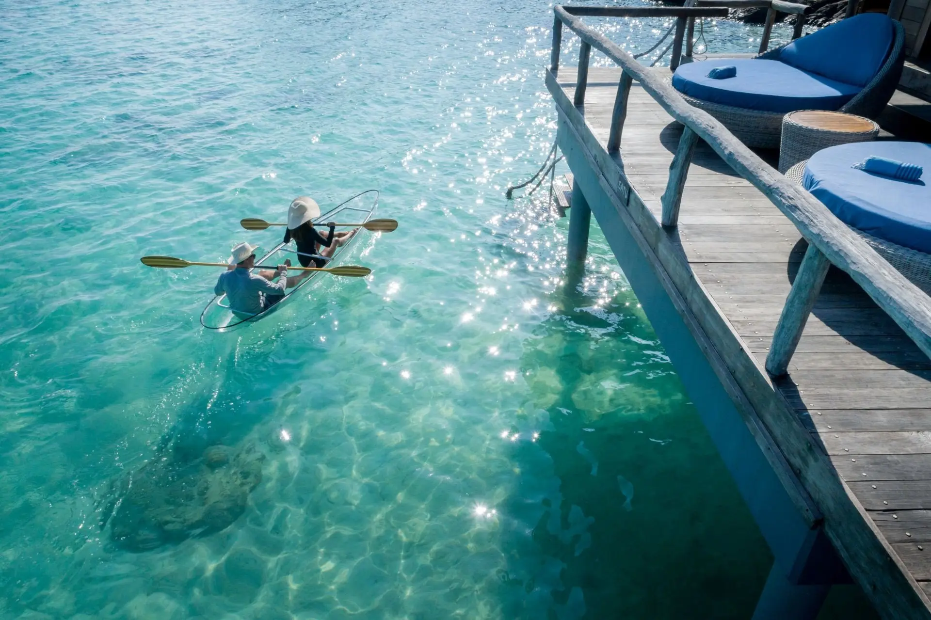 close_up_backview_young_couple_clear_kayaking_in_lagoon_under_overwater_suite_sun_terrace